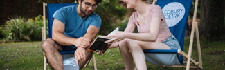 A male and female sitting on Ledbury Poetry branded deckchairs and reading a book together