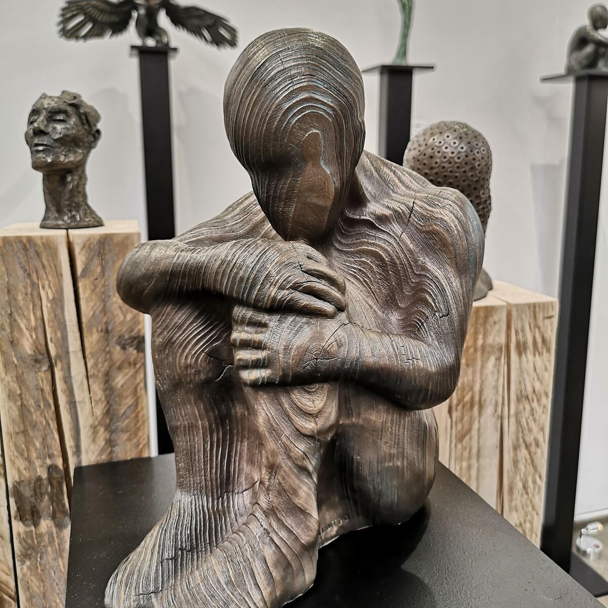 wooden carved sculpture of a person sitting holding their knees to their chest