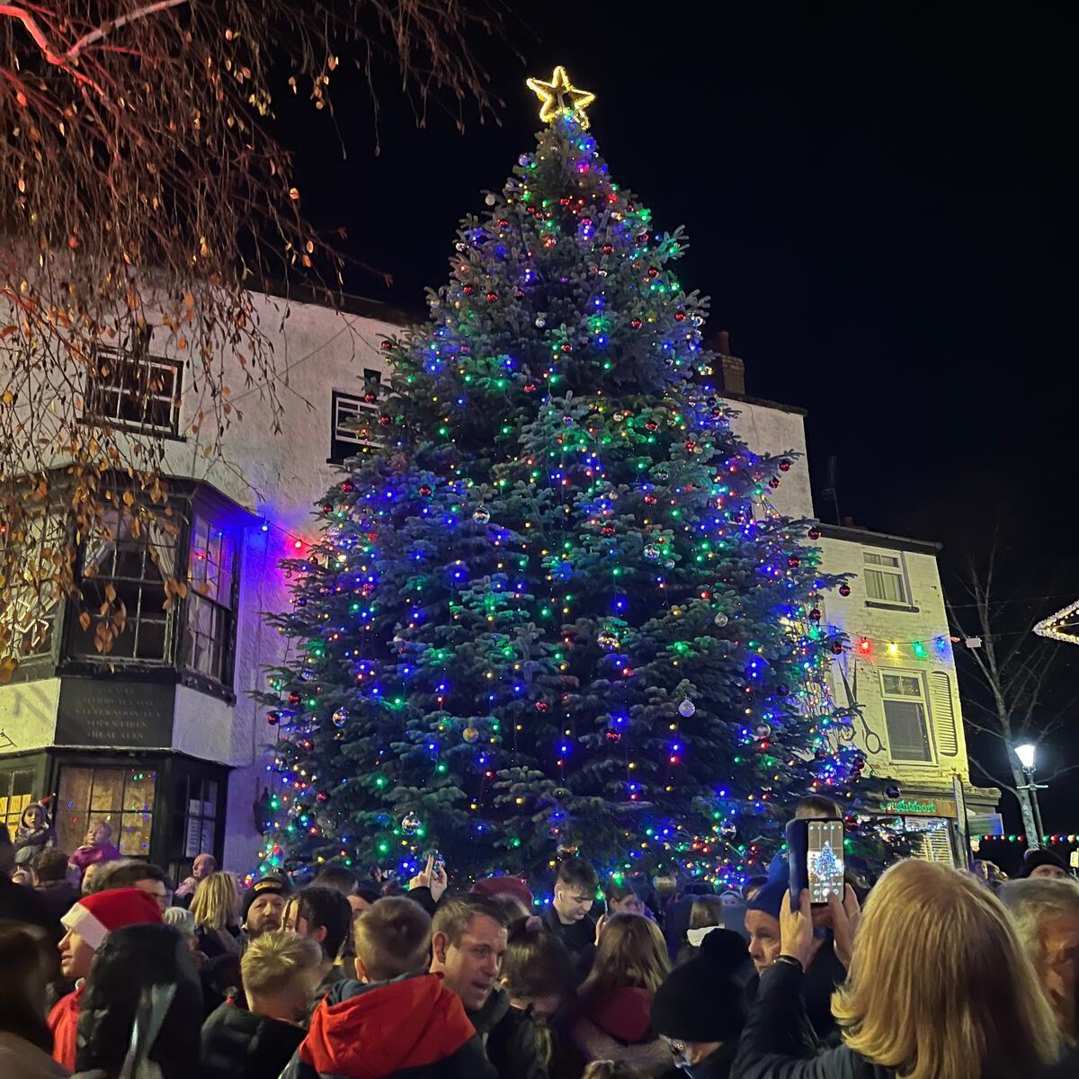 large decorated Christmas tree in town square with crowds