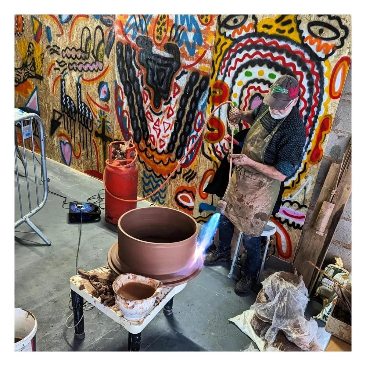 Man with blowtorch and large red clay pot on potter's wheel