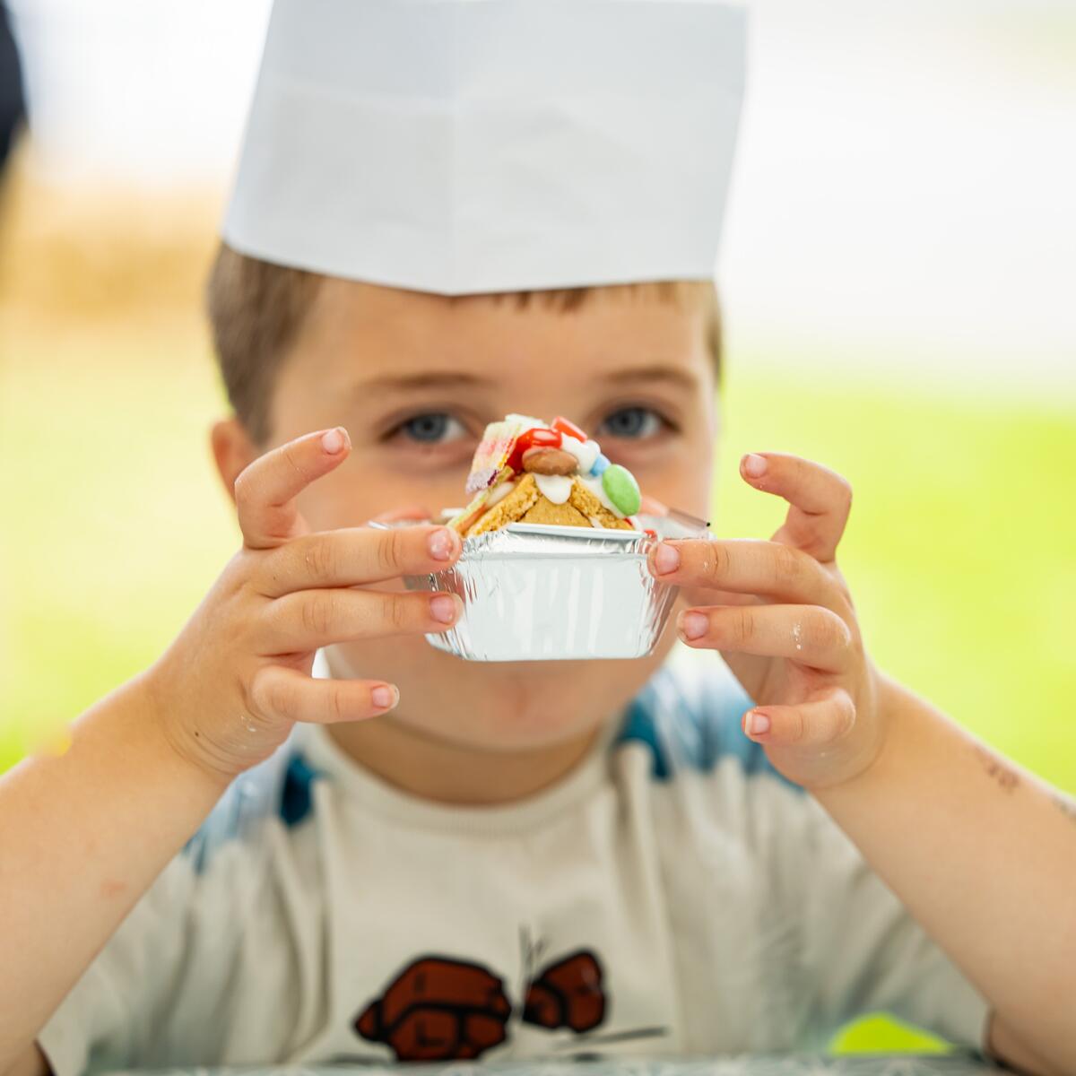 Child wearing a chefs hat holding a sweet creation