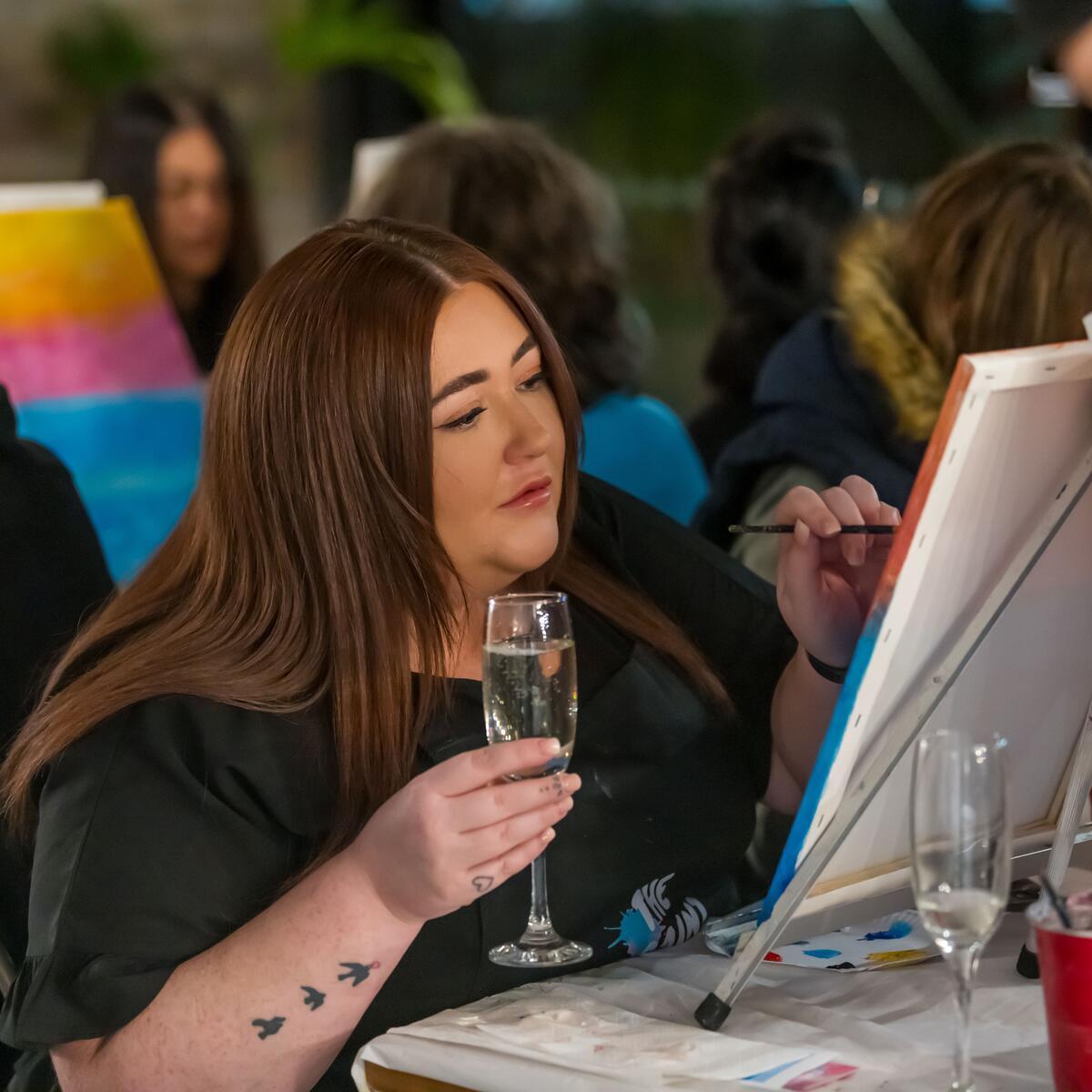 Person holding glass of bubble sat in front of a canvas painting