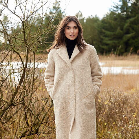 Woman with long brown hair in thick cream coloured winter coat outdoors