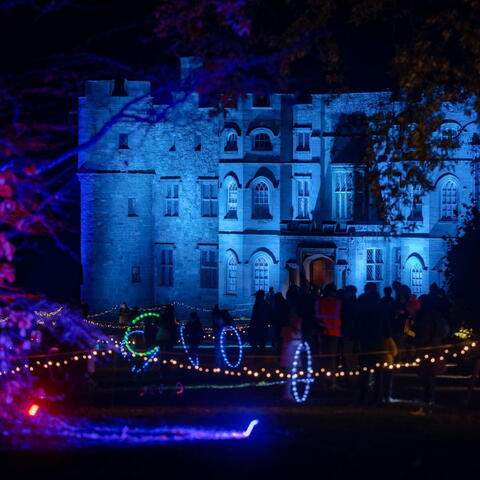 Croft castle illuminated with blue  light projections on castle walls and coloured lights in trees