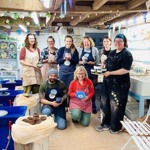 A group of people holding hand made posts at a pottery course