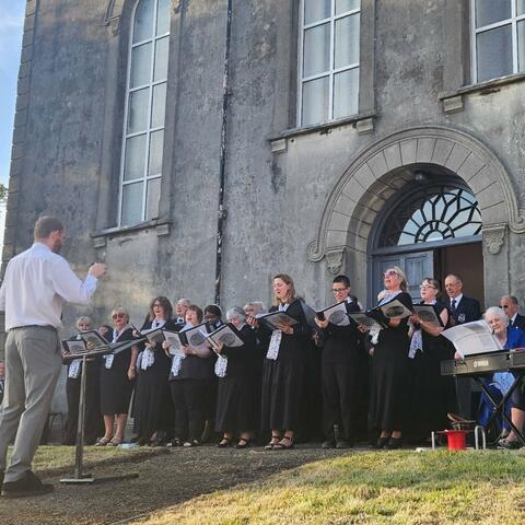 Large choral group outside big grey building 