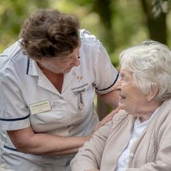 woman in carers uniform speaking to an elderly lady in a wheelchair