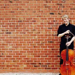 Robin Michael standing in front of a brick building with a cello 