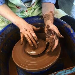 hands on a clay pot on a potter's wheel