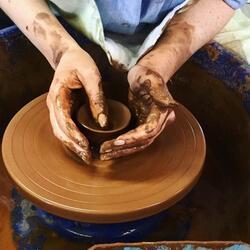 hands on a clay pot on a potter's wheel